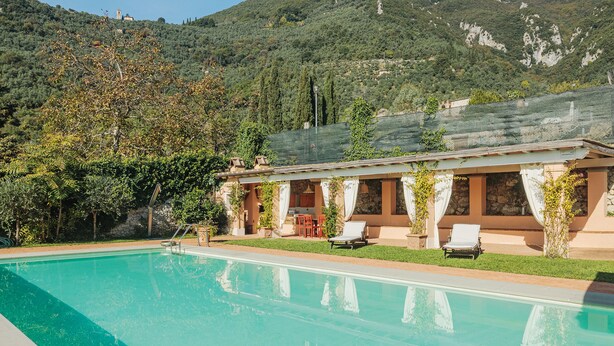 A poolside area with a clear view of a mountain backdrop, a building with a covered patio, and a swimming pool. - Villa / Independent home in Lucca with 9 bedrooms sleeps 18 (Lucca)