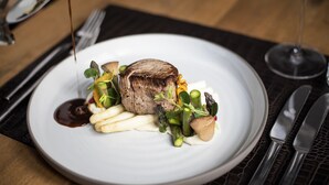 A white plate with a piece of meat, vegetables, and sauce. - Essgold (Ratingen)