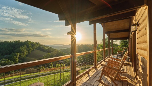Una terraza de madera con vistas a un valle, una barandilla y una mesa.