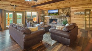 Una sala de estar acogedora con chimenea de piedra, sofás de cuero y un ventilador de techo.