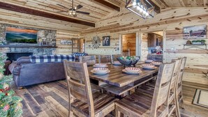 Un acogedor interior de cabaña de troncos con comedor, chimenea y un árbol de Navidad.