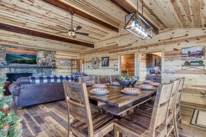 A cozy log cabin interior with a dining area, fireplace, and a Christmas tree.