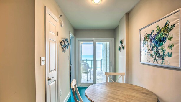 A hallway leading to a balcony with a view of the ocean, a round wooden table, and a chair. - Direct Beach Access: North Myrtle Condo! (North Myrtle Beach)