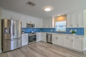 A modern kitchen with white cabinets, stainless steel appliances, and blue-tiled backsplash.