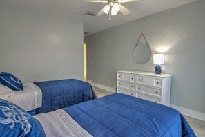 A bedroom with two beds, a ceiling fan, a dresser, and a wall-mounted mirror.