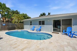 Une piscine dont le bord est revêtu de carrelage, entourée d’une terrasse avec des chaises et une clôture en bois.