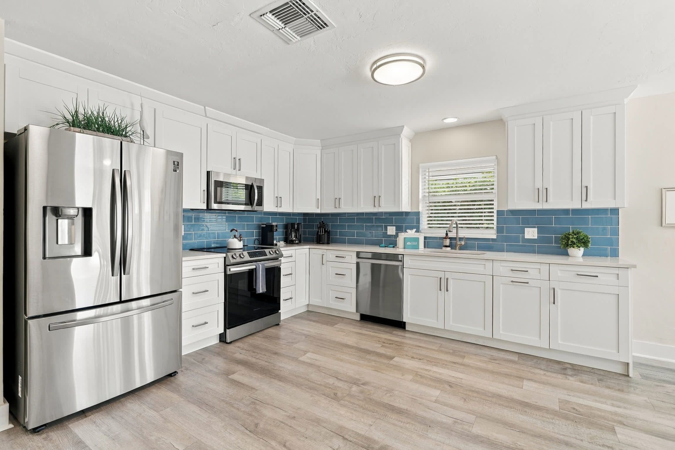 A modern kitchen with white cabinetry, stainless steel appliances, a blue tiled backsplash, and a wooden floor.