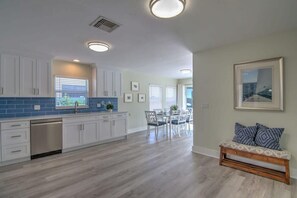 A modern kitchen with white cabinets, blue backsplash, and a dining area with a bench and chairs.