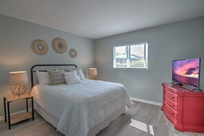 A bedroom with a bed, two bedside tables with lamps, a dresser, a television, and a window with blinds.