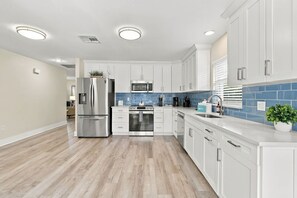 A modern kitchen with white cabinetry, a stainless steel refrigerator, a microwave, and a dishwasher. - Beach-Inspired Naples Park Home | Heated Pool (Naples)