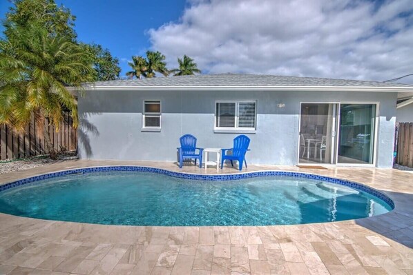 Una piscina con azulejos azules, dos sillas azules y una pequeña mesa.