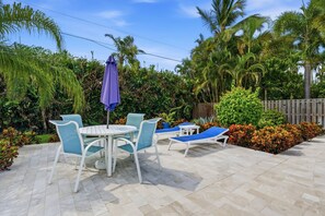 A patio with a table and chairs, a small table, and lounge chairs. - Beach-Inspired Naples Park Home | Heated Pool (Naples)
