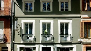 A two-story building with a balcony on the second floor, a door with a small step leading up, and a window with a metal grill.