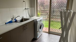 A laundry area with a washing machine, a sink, and a window overlooking a garden. - Shore to Impress (Inverloch)