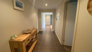 A hallway with a wooden bench, a framed picture on the wall, and a door at the end. - Shore to Impress (Inverloch)