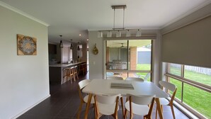 A modern kitchen with a dining area, large windows, and a view of the backyard. - Shore to Impress (Inverloch)