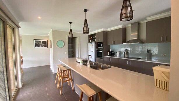 A modern kitchen with a large island, stainless steel appliances, and pendant lighting. - Shore to Impress (Inverloch)