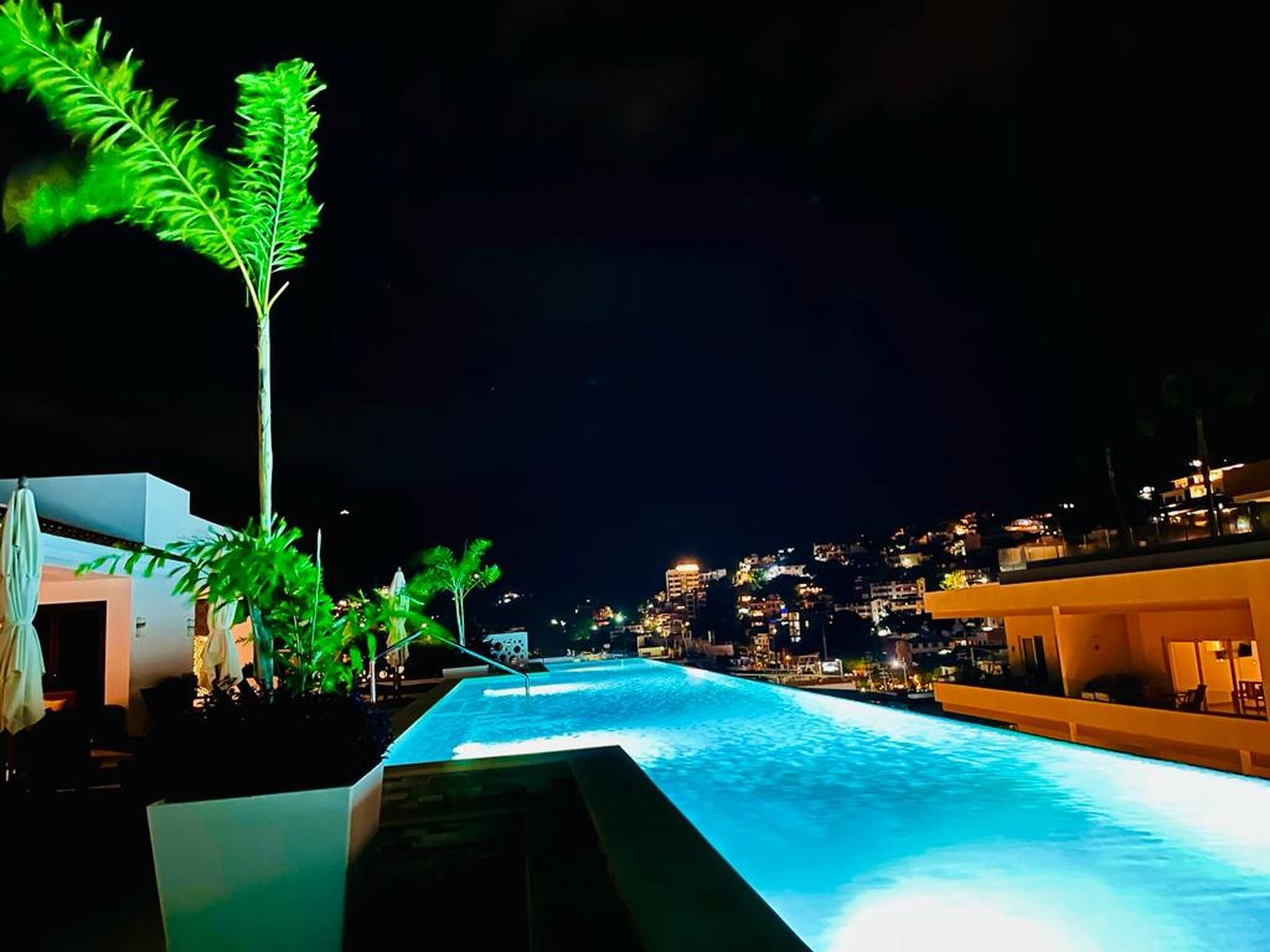 Une piscine illuminée la nuit, avec une vue sur la ville en arrière-plan.