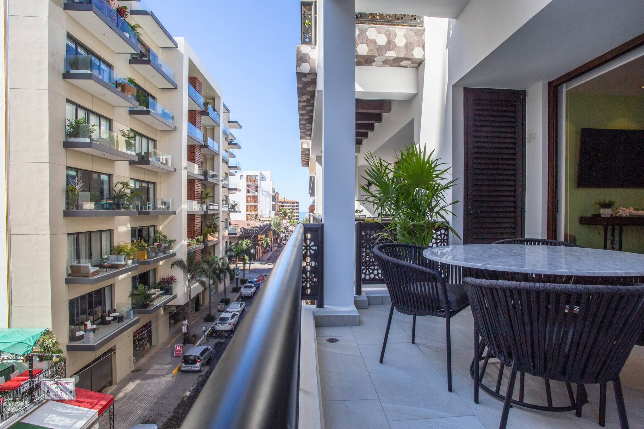 A balcony with a table and chairs, overlooking a street with parked cars and buildings.