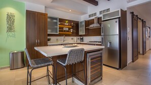 Een moderne keuken met een centraal eiland, barstoelen, een roestvrijstalen koelkast en houten keukenkastjes.