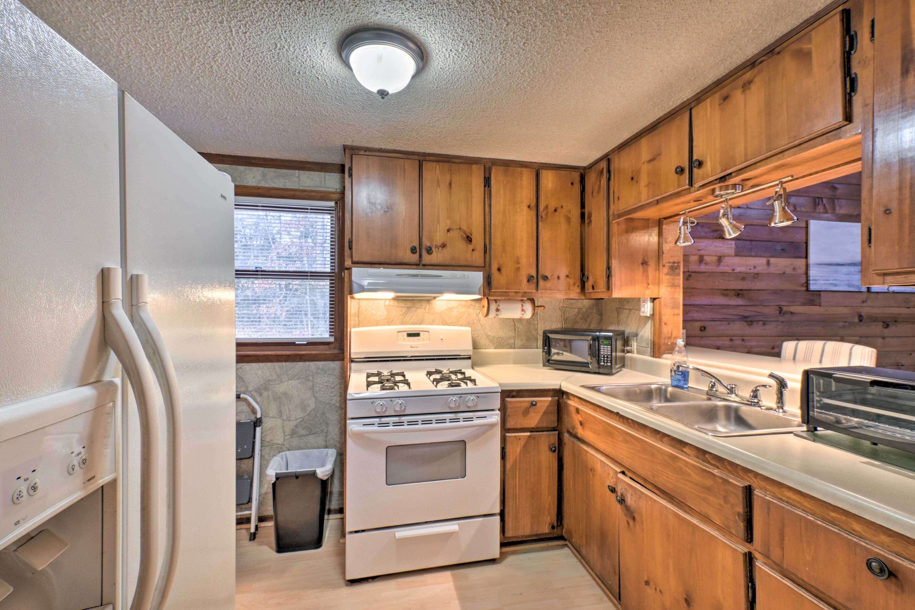 Une cuisine de taille réduite, avec des meubles en bois, une cuisinière blanche, un four à micro-ondes et un évier.