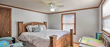 A bedroom with a wooden bed, a ceiling fan, a window with blinds, and a desk with a map.