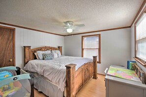 Ein Schlafzimmer mit einem hölzernen Bett, einem Deckenventilator, einem Fenster mit Jalousien und einem Schreibtisch mit einer Karte.