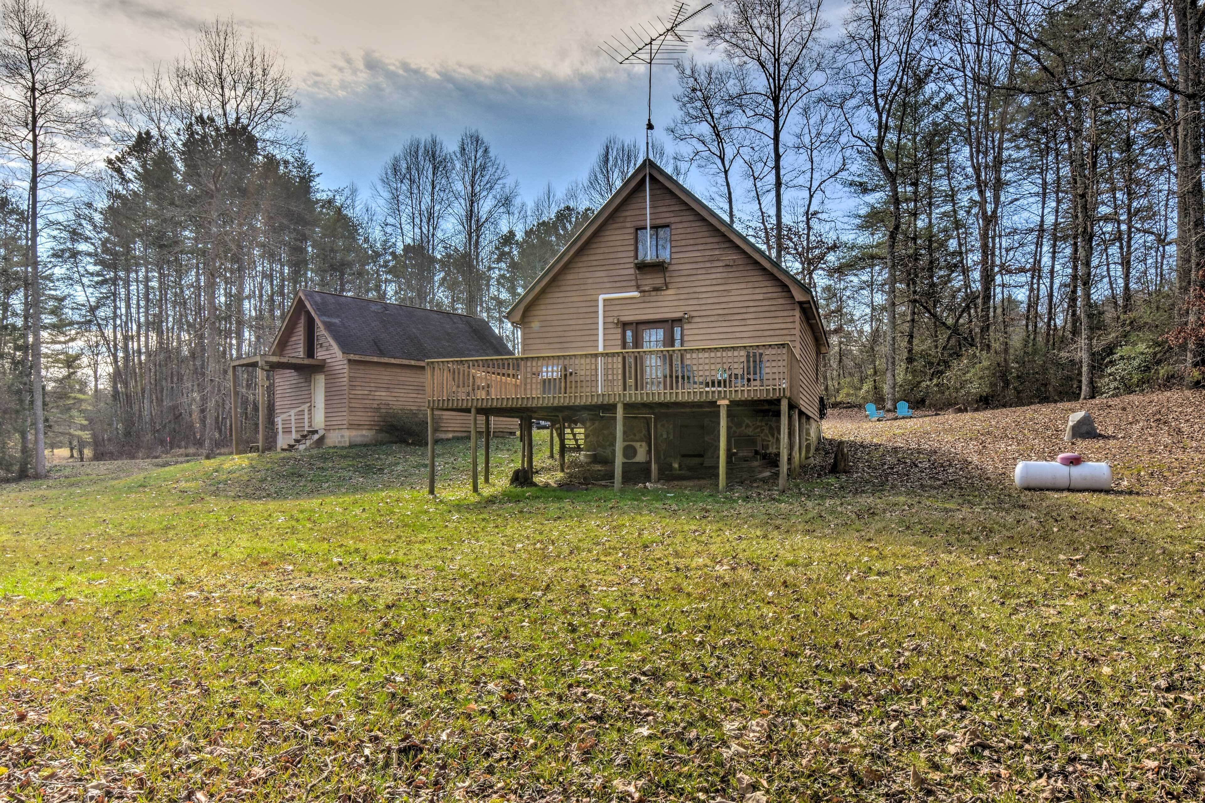A wooden cabin with a balcony, surrounded by a forested area.
