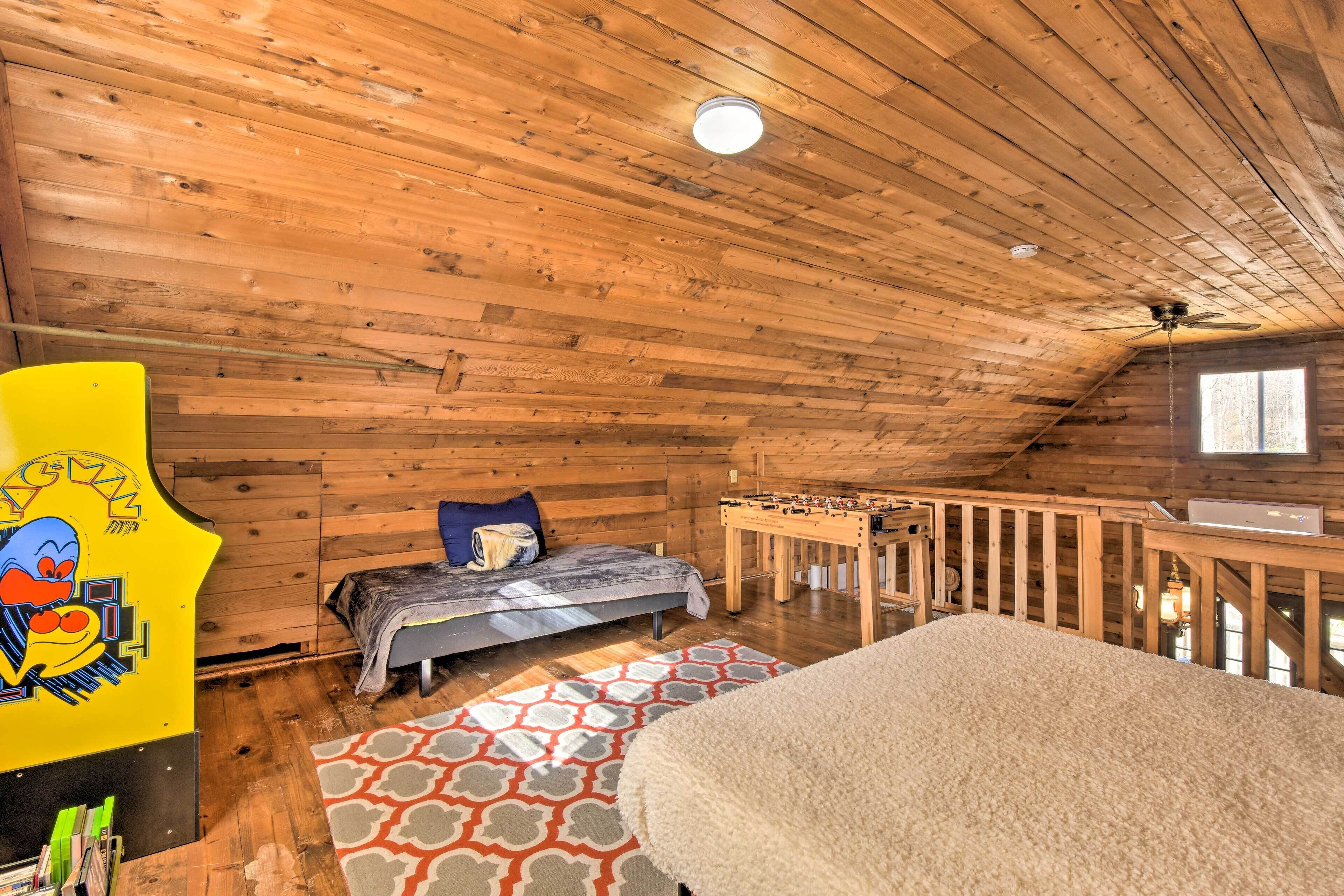 Ein gemütliches Schlafzimmer im Dachgeschoss mit Holzwänden und schrägen Decken, mit einem Bett, einem Kicker und einem Fenster, das für natürliches Licht sorgt.