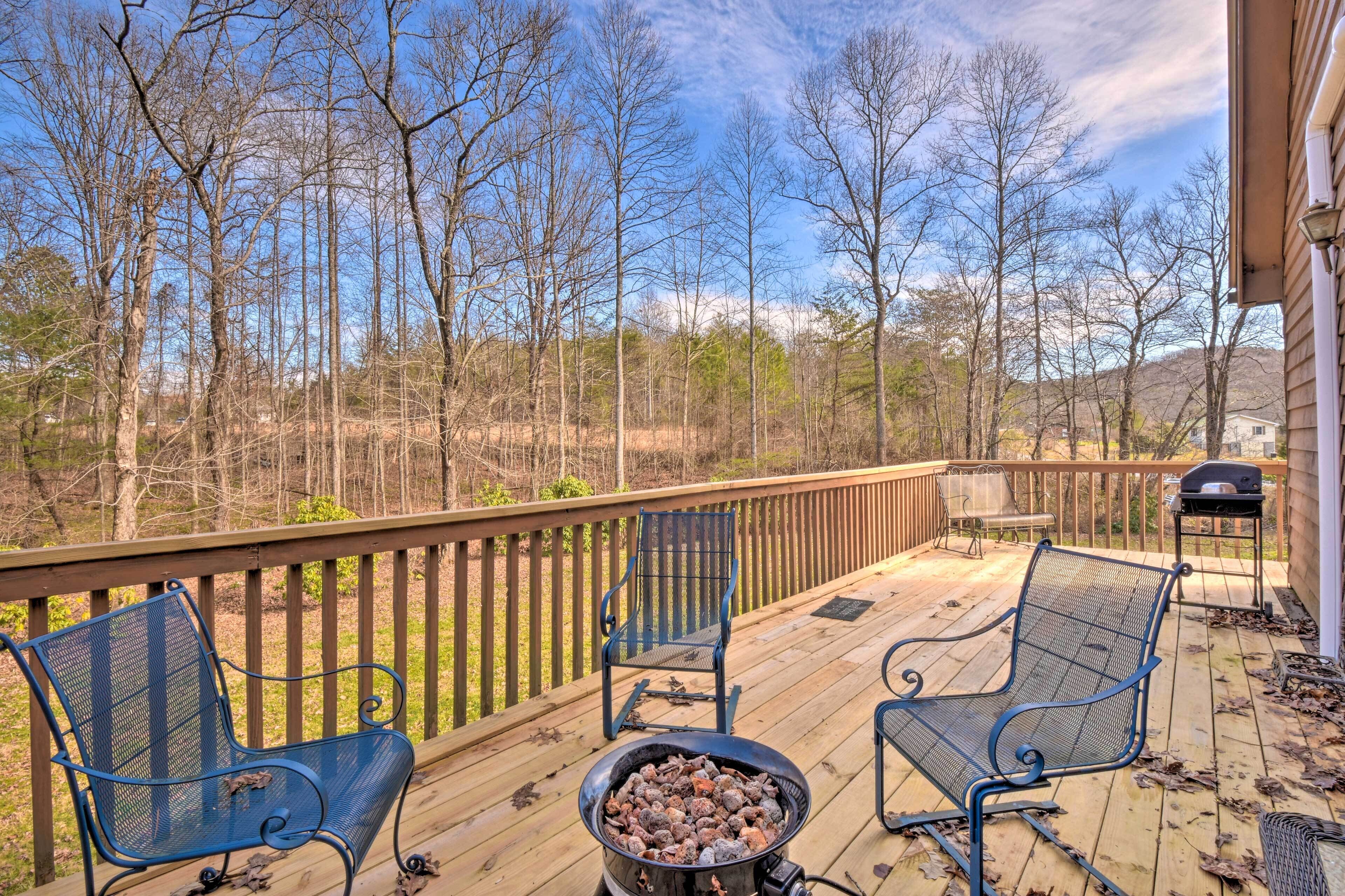 A wooden deck with two blue metal chairs and a grill.