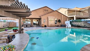 A pool area with a curved design, a pergola, outdoor seating, and a building with a balcony. - Maricopa Home w/ Swim-Up Bar, Heated Pool & Slide (Maricopa)