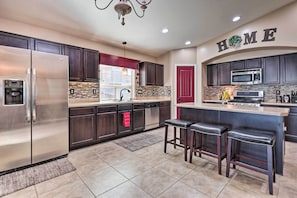A modern kitchen with dark wood cabinets, stainless steel appliances, and a bar area with stools.