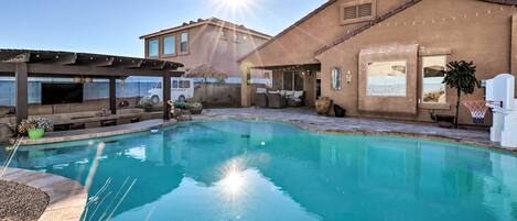A swimming pool with a pergola and outdoor seating area, surrounded by buildings and a basketball hoop.