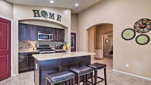 A kitchen with dark cabinets, a stainless steel microwave, a large island with bar stools, and a 'HOME' sign above the entrance. - Maricopa Home w/ Swim-Up Bar, Heated Pool & Slide (Maricopa)