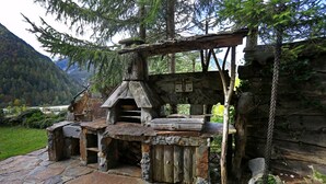 Un área de cocina al aire libre de estilo rústico, con suelo de piedra y estructuras de madera, rodeada de un paisaje montañoso.
