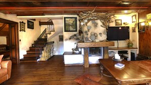 Un salón con suelo de madera, chimenea, televisor y escalera.
