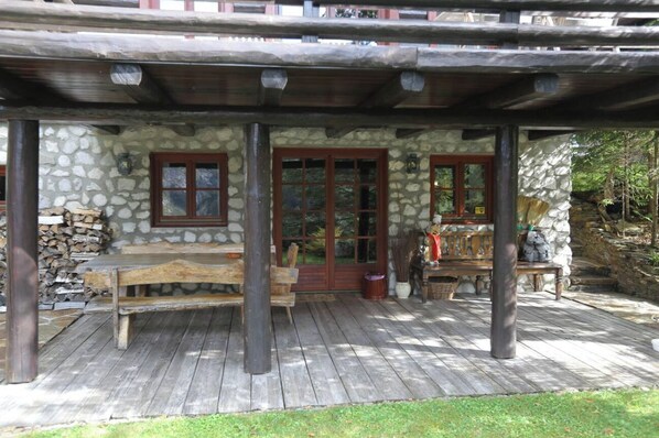 Un bâtiment rustique en pierre, doté d’une terrasse en bois, de murs en pierre et d’un banc en bois.