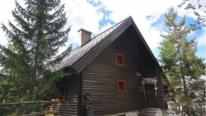 Una cabaña de troncos con techo inclinado, dos ventanas y una chimenea de piedra.
