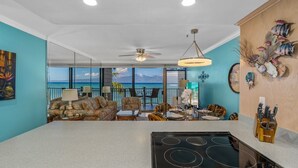 Une cuisine moderne dotée d’un grand îlot central, d’un coin repas offrant une vue agréable et d’un salon équipé d’un ventilateur de plafond.