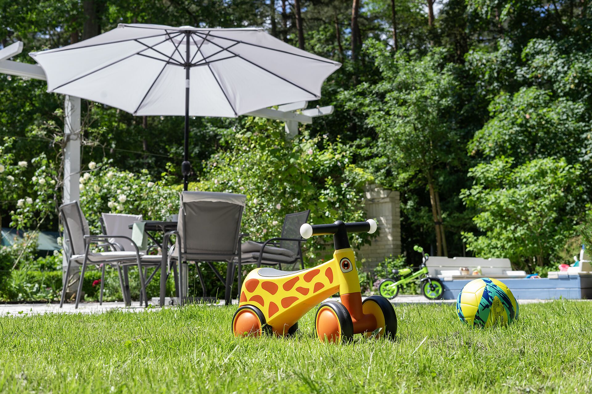 Un espace extérieur recouvert d’herbe, avec un jouet automobile jaune, un ballon de plage et un parasol blanc.