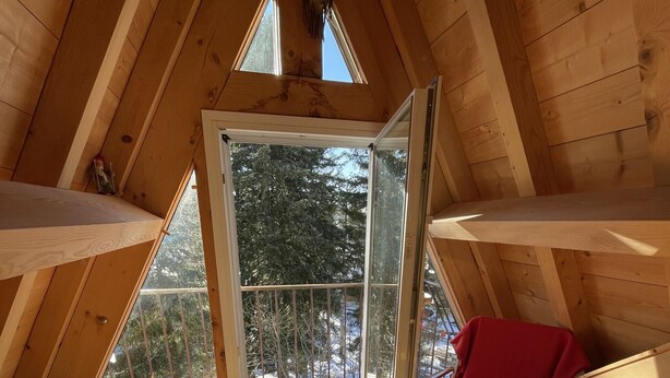 Una habitación de ático acogedora con una silla roja, suelo de madera y vistas a árboles a través de un gran ventanal.