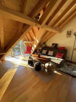 Acogedor dormitorio en el ático con vigas de madera, un sofá, un sillón rojo y una mesita.