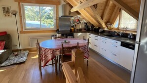 Un dormitorio acogedor en el ático, con techo de madera, un ventanal grande y una zona de comedor con mesa y sillas.