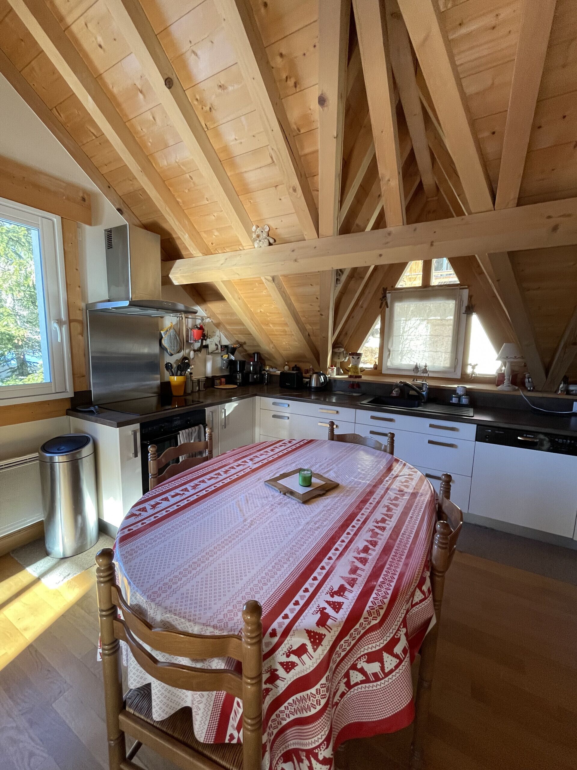 A cozy kitchen with wooden beams, a stainless steel refrigerator, and a dining table with a patterned tablecloth.