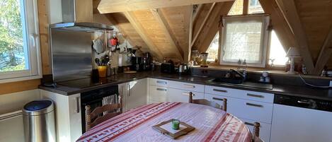 A cozy kitchen with wooden beams, a stainless steel refrigerator, and a dining table with a patterned tablecloth.