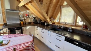 Una cocina acogedora con vigas de madera, un refrigerador de acero inoxidable, armarios blancos y un mantel rojo estampado.