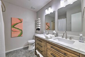 Un baño moderno con un inodoro blanco, un tocador de madera con un espejo grande y dos lavabos.
