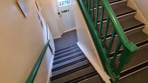 Una escalera con barandales verdes que lleva a una puerta con la inscripción 'FIRE EXIT'.