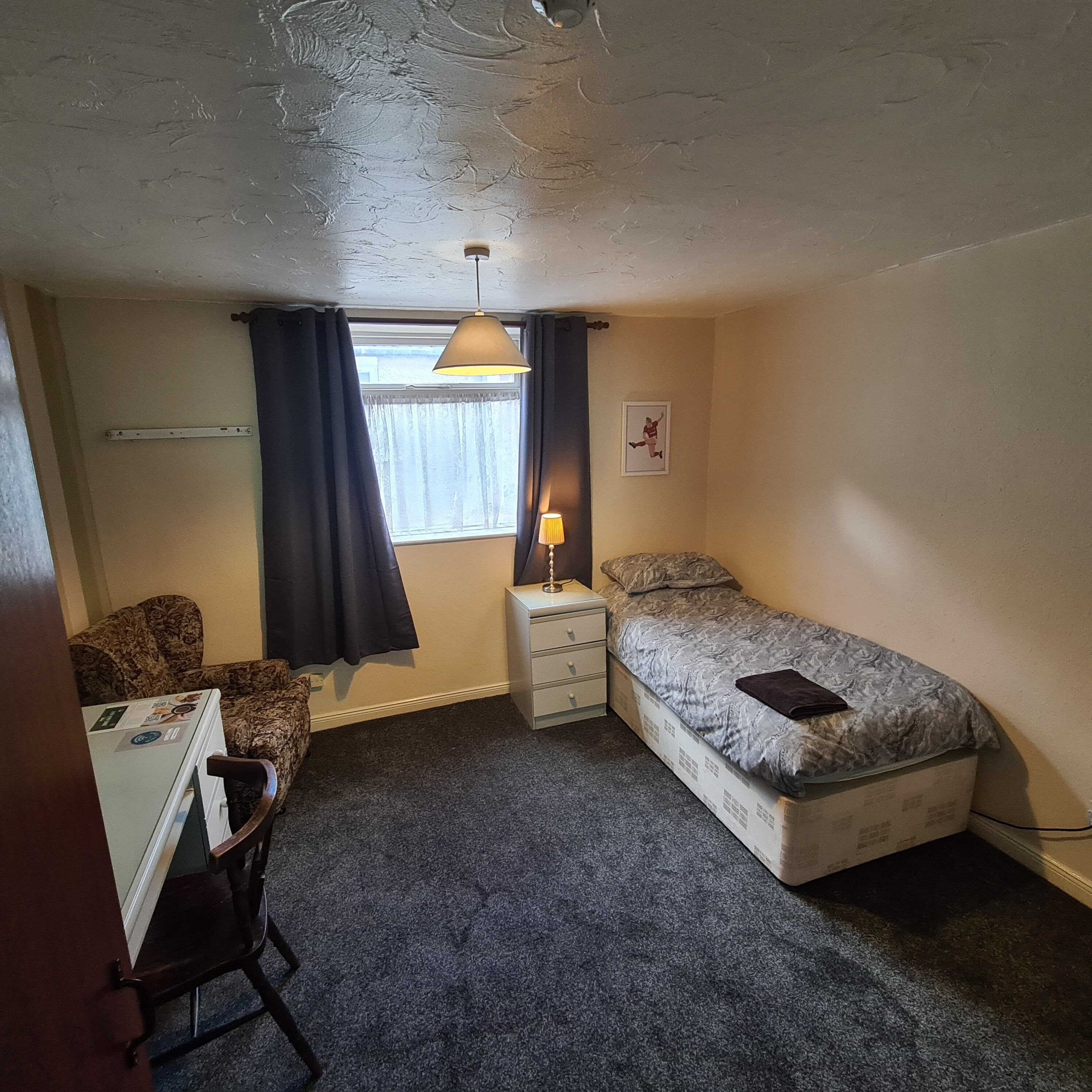 A compact room with a desk, a bed, and a window with curtains.