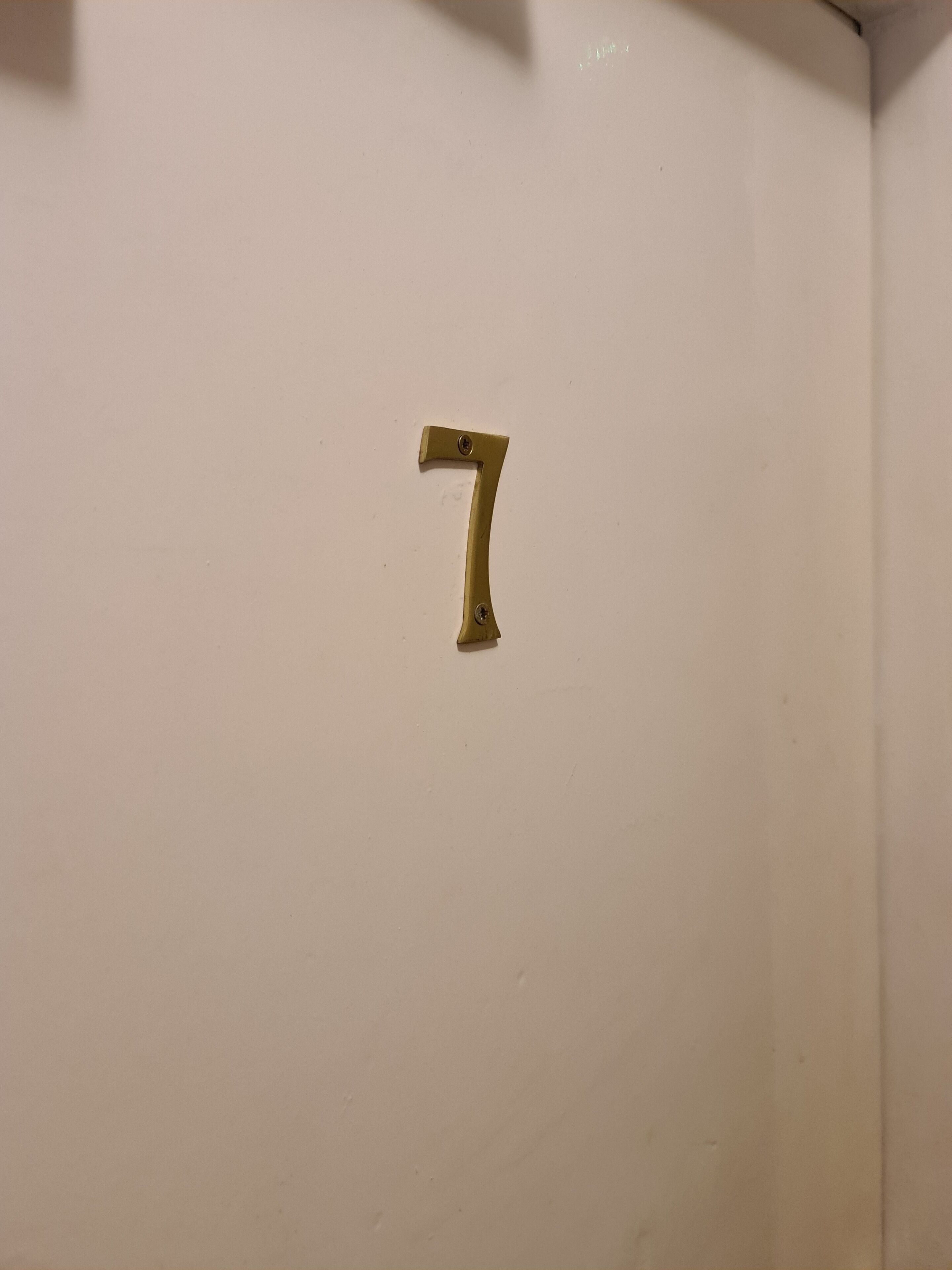 A brass door handle with the number 7 on a white door.